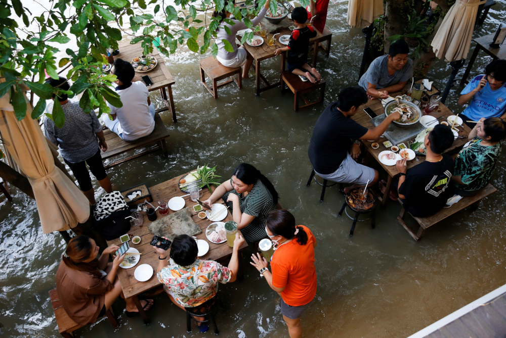 People eat food at a flooded restaurant, where patrons stand up from their tables every time the waves come in, on a river bank in Nonthaburi near Bangkok, Thailand, October 7, 2021. u00e2u20acu201d Reuters picnn