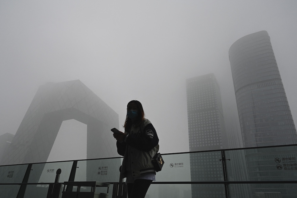 A woman uses her phone along a glass wall with the China Central Television (CCTV) headquarters in the background on a polluted day in Beijing November 5, 2021. u00e2u20acu201d AFP pic