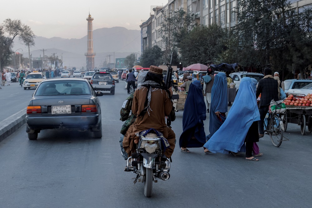 A group of women wearing burqas crosses the street as members of the Taliban drive past in Kabul, Afghanistan October 9, 2021. u00e2u20acu2022 Reuters file pic