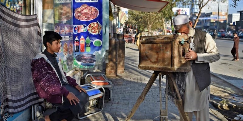In this photograph taken on October 13, 2021, Afghan photographer Haji Mirzaman (right) takes a portrait of a boy with his homemade wooden box camera known as a u00e2u20acu02dckamra-e-faoreeu00e2u20acu2122 on a sidewalk in Kabul.. u00e2u20acu2022 ETX Studio picnn
