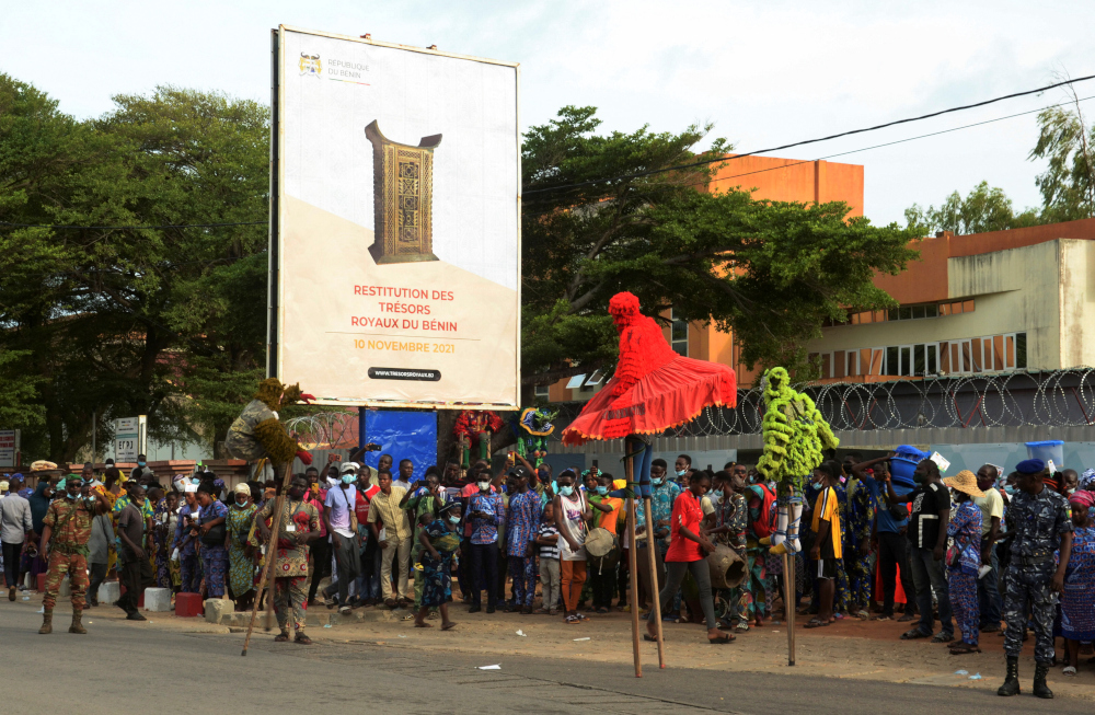 People wait to welcome the convoy carrying 26 cultural artefacts stolen from the Kingdom of Abomey during the colonial era, in a street of Cotonou, Benin November 10, 2021. The Billboard reads u00e2u20acu02dcReturn of the royal treasures of Beninu00e2u20acu2122. u00e2u20acu201d Reuters pic