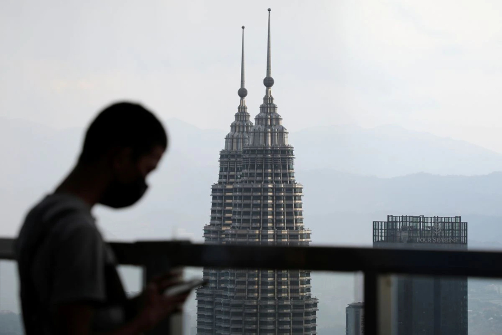 A man wearing a protective mask uses his phone as the Petronas Twin Towers are seen in the background in Kuala Lumpur, Malaysia April 12, 2021. u00e2u20acu201d Reuters picn