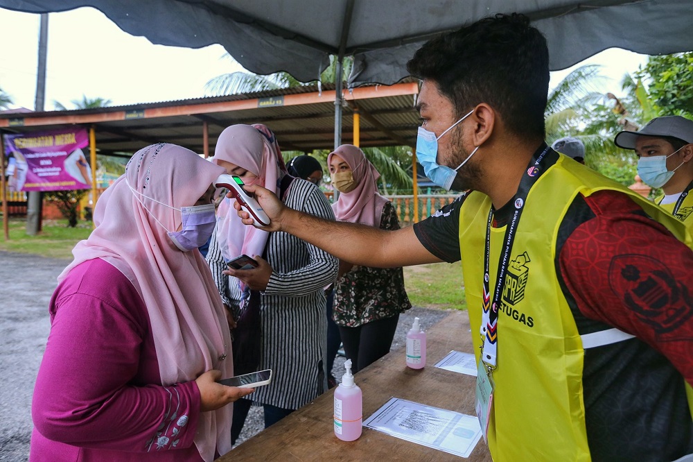 An Election Commission staff takes the temperature of a voter at the SK Durian Daun (K) polling centre in Melaka, November 20, 2021. u00e2u20acu201d Picture by Ahmad Zamzahuri