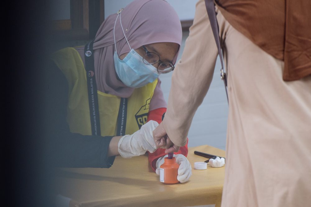 An Election Commission officer dips a voteru00e2u20acu2122s finger in indelible ink during the Melaka state election at the Durian Tunggal polling station in Melaka November 20, 2021. u00e2u20acu201d Picture by Shafwan Zaidon