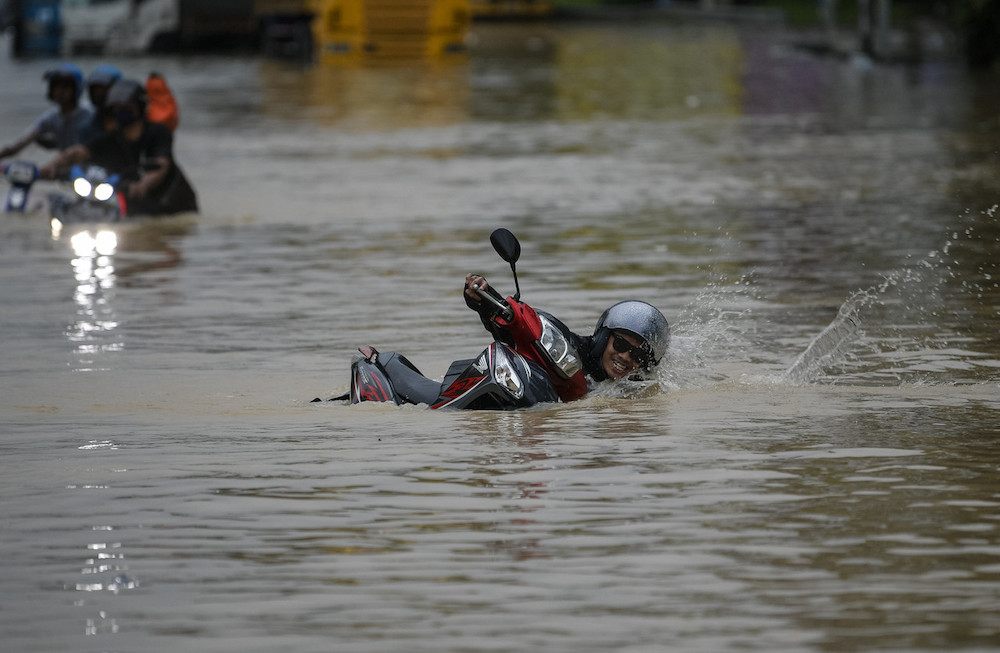 A motorcyclist falls while navigating the flooded Federal Highway, December 18, 2021. u00e2u20acu201d Bernama pic