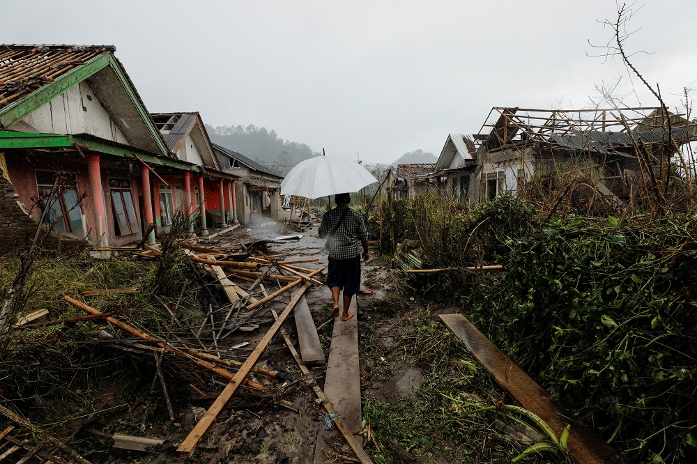 A man with an umbrella walks amongst damaged houses looking for his goat in an area affected by the eruption of Mount Semeru volcano in Curah Kobokan, Pronojiwo district, Lumajang, Indonesia December 6, 2021. u00e2u20acu201d Reuters pic