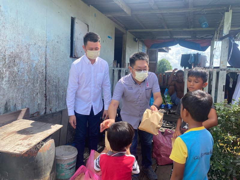Hee helps to distribute Christmas presents to children at a squatter area as Ling (left) looks on. u00e2u20acu201d Borneo Post pic