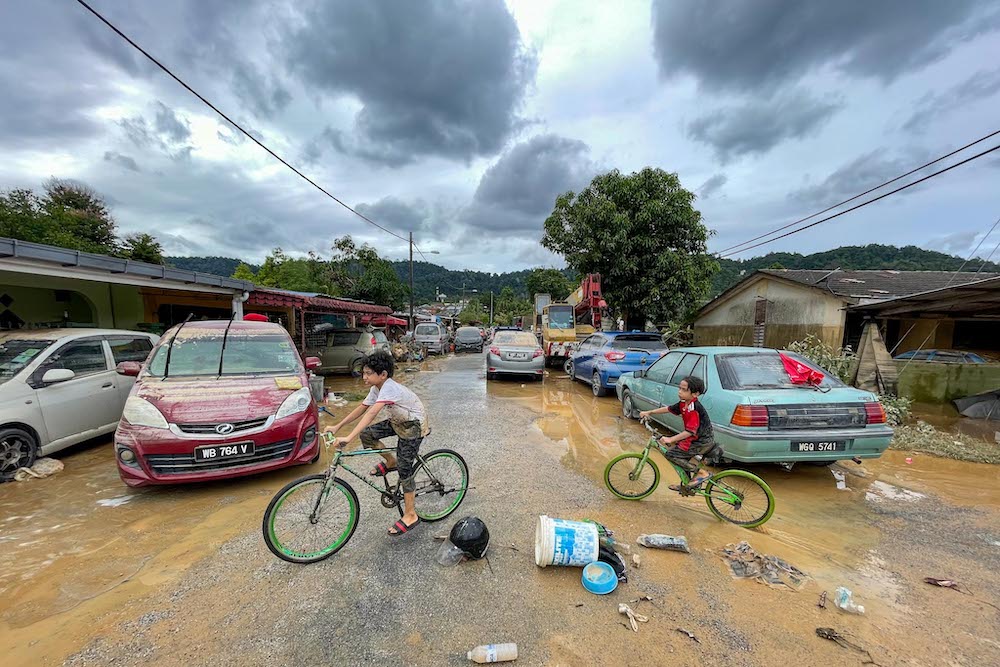 Children are seen on their bicycles on the mud-filled streets of Hulu Langat December 19, 2021. — Picture by Hari Anggara 