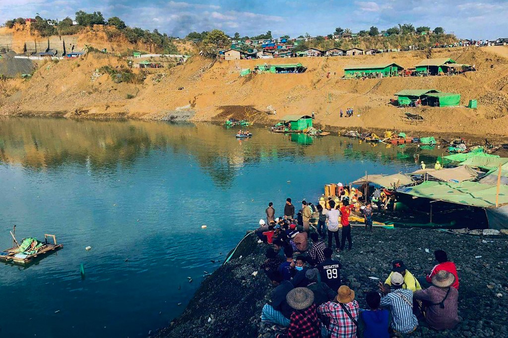 This photo taken and received via an anonymous source on December 22, 2021 shows onlookers watching as rescue officials search for missing people after a landslide at a jade mine in Hpakant, Kachin state. u00e2u20acu201d Handout via AFP