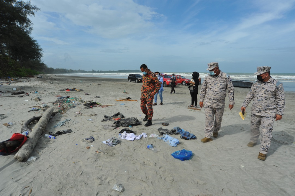Malaysian Maritime Enforcement Agency (MMEA) and Fire and Rescue Department personnel scouring through the victim’s personal items strewn along the Tanjung Balau beach in Kota Tinggi, December 15, 2021. — Picture by Ben Tan