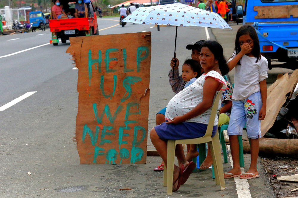 A family displays signage as they ask for alms along a highway in Surigao City, Surigao del Norte province on December 25, 2021, more than a week after Super Typhoon Rai devastated the province. u00e2u20acu201d AFP pic 