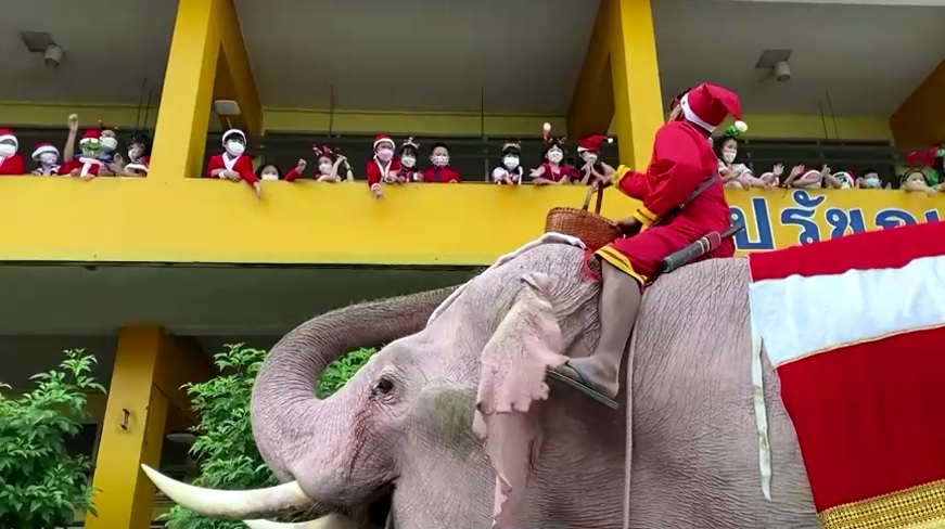 A man in a Santa suit riding an elephant throws candy to schoolchildren at a school in Thailand December 24, 2021. u00e2u20acu201d Reuters video screencap