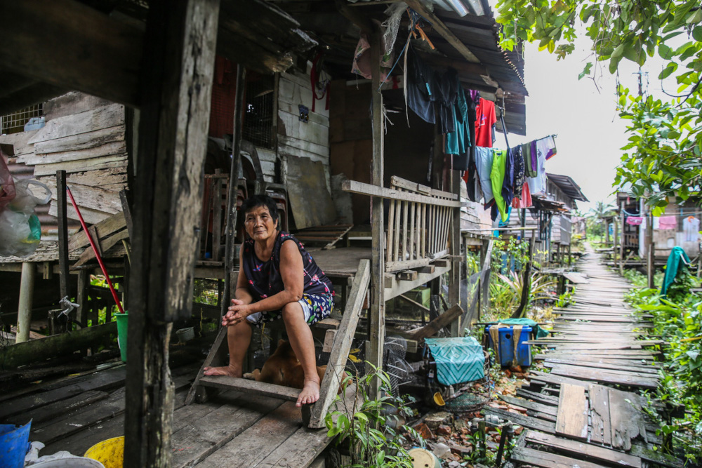 An elderly woman poses for a picture in front of her home at Kampung Kudei in Satok December 10, 2021. 