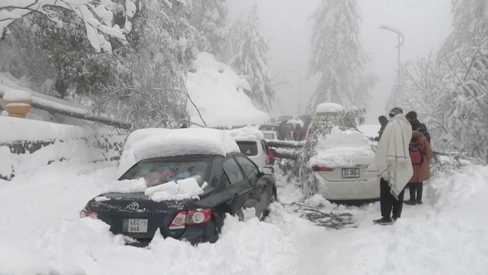 People stand next to cars stuck under fallen trees on a snowy road, in Murree, northeast of Islamabad, Pakistan in this still image taken from a video January 8, 2022. u00e2u20acu201d PTV/Reuters TV via Reuters
