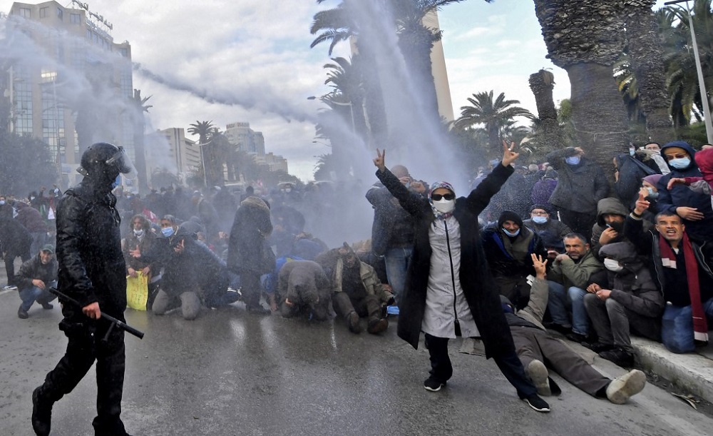 A Tunisian demonstrator flashes the V for victory sign as police fire water cannons during protests against President Kais Saied, on the 11th anniversary of the Tunisian revolution in the capital Tunis January 14, 2022. u00e2u20acu201d AFP pic