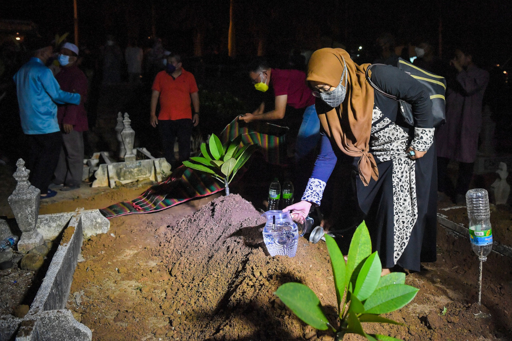 Siti Amirah pours water over her fatheru00e2u20acu2122s grave, Pahang Mentri Besar press secretary Datuk Abdul Wahab Mohamad Ali, at the Bukit Ubi Muslim Cemetery in Kuantan, January 11, 2022. u00e2u20acu201d Bernama pic 