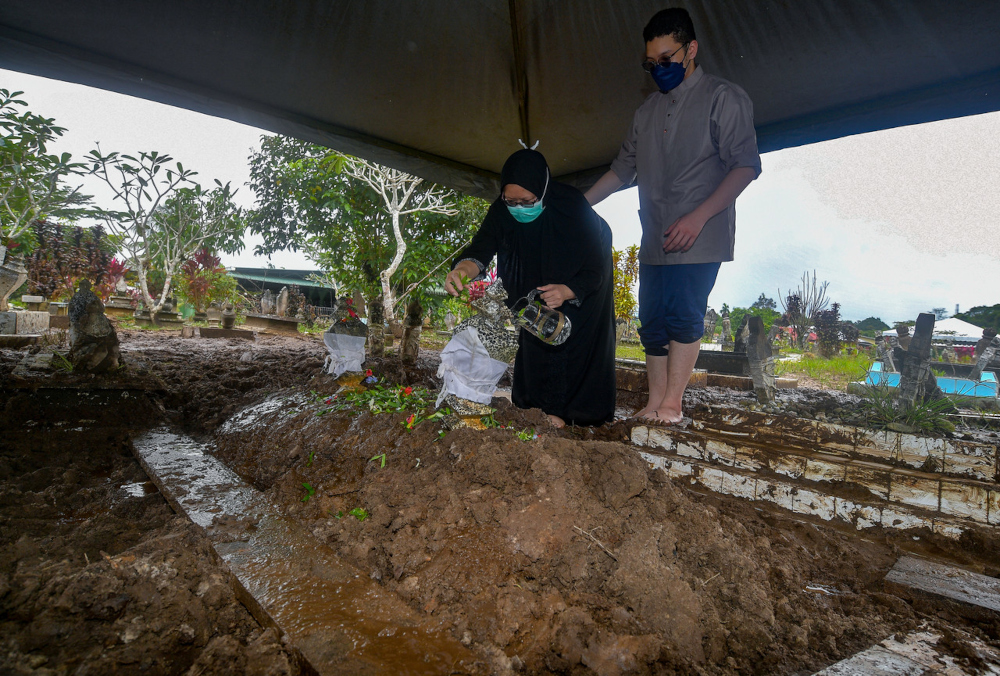 Dayang Farezah Abang Mustapha with her son Hazim Izzuddin Jumaat (right) at the grave of their uncle Tan Sri Mohamad Jemuri Serjan, at the Kampung Pinang Jawa Islamic Cemetery in Kuching, January 26, 2022. u00e2u20acu201d Bernama pic 