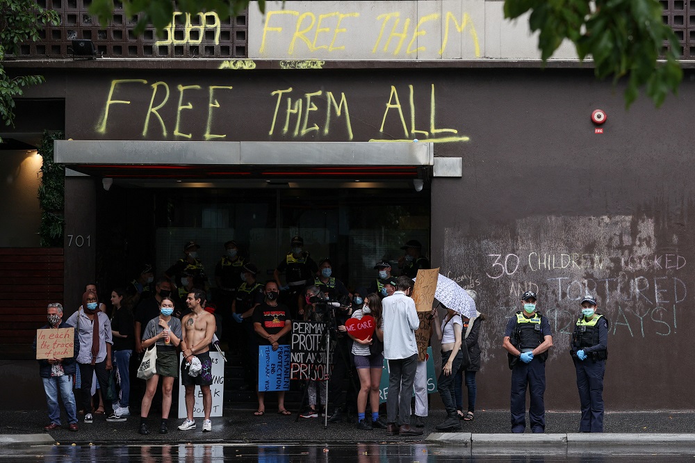 Pro-refugee protestors and police officers stand together under an awning at the entrance to the Park Hotel, where Serbian tennis player Novak Djokovic is believed to be held while he stays in Australia, in Melbourne, Australia January 7, 2022. u00e2u20acu2022 Reuter