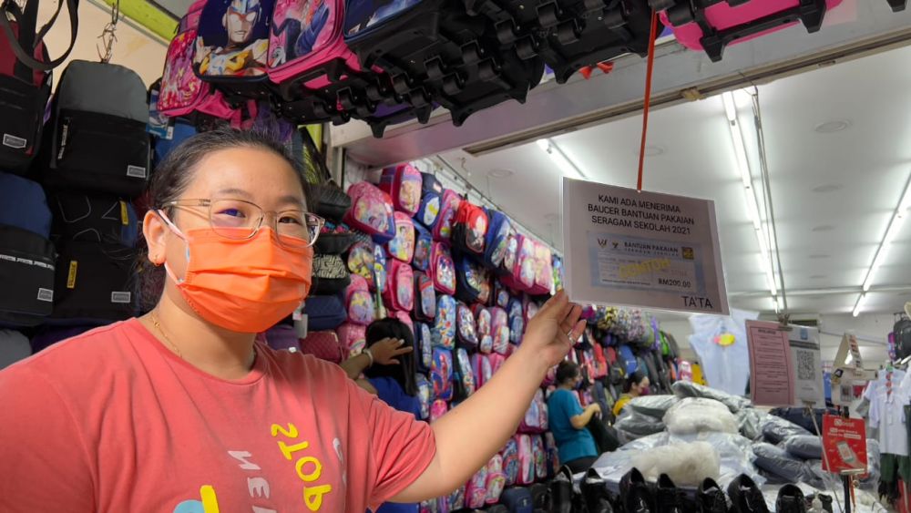 Jong shows the display card informing shoppers that her shop accepts the Sarawak Foundation’s RM200 voucher, which can be used to redeem school supplies worth the same value. — Picture by Roystein Emmor/ Borneo Post