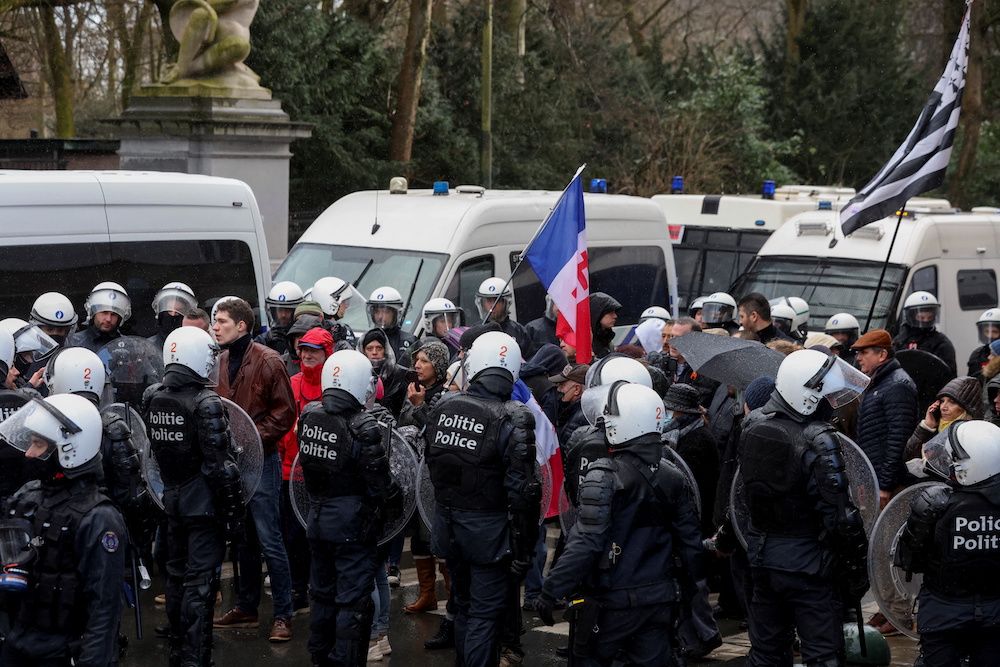 Police officers in riot gear stand next to demonstrators during a protest near EU institutions headquarters against coronavirus disease (Covid-19) restrictions, in Brussels, Belgium February 14, 2022. u00e2u20acu201d Reuters picnn