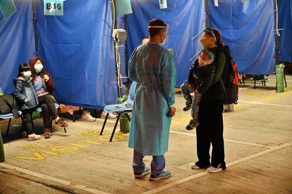 A woman (right) with her child talks to a medic as they prepare to spend the night with temperatures falling outside the Caritas Medical Centre in Hong Kong February 16, 2022. — AFP pic