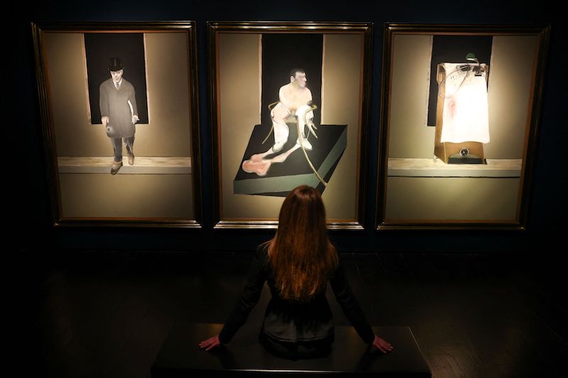 A gallery assistant poses by an artwork titled 'Triptych 1986-7' by Francis Bacon ahead of u00e2u20acu02dc20th / 21st Century and Art of the Surreal Evening Saleu00e2u20acu2122 auction at Christie's in London February 23, 2022. u00e2u20acu201d Reuters pic