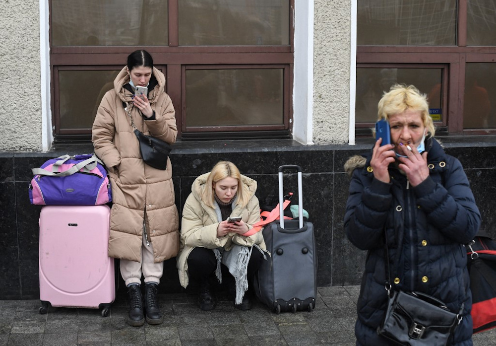 Women use their phone as they wait with bags and suitcases near Kyiv-Pasazhyrskyi railway station in Kyiv in the morning of February 24, 2022. u00e2u20acu201d AFP pic
