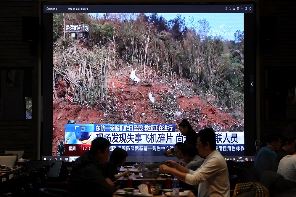 A screen shows news footage of plane debris at the site where a China Eastern Airlines Boeing 737-800 plane flying from Kunming to Guangzhou crashed in Wuzhou, while customers dine at a restaurant in Beijing March 22, 2022. u00e2u20acu201d Reuters pic