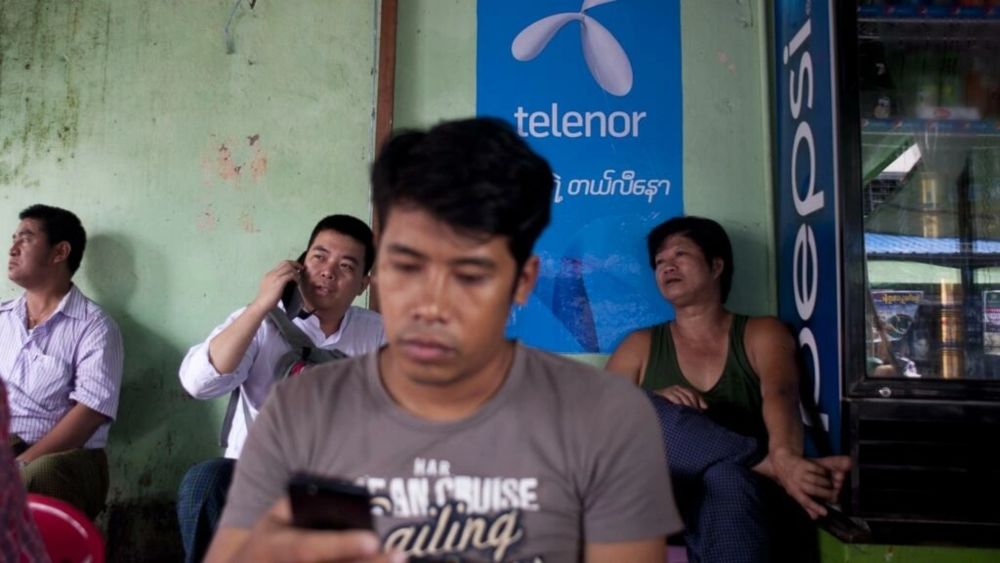 A man uses a phone in front of a Telenor advertising board in Yangon. u00e2u20acu201d AFP file pic