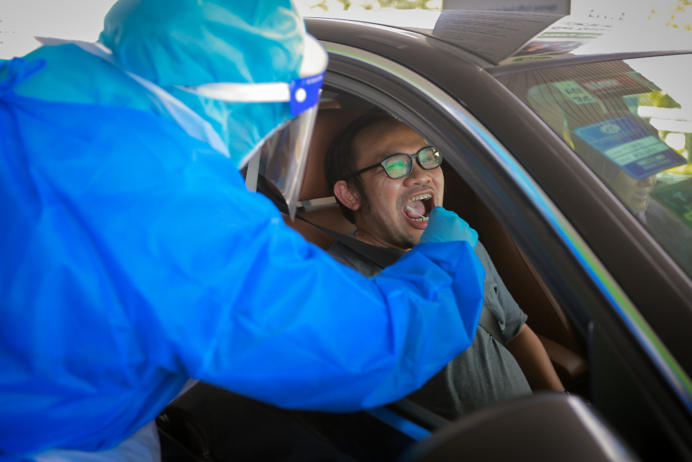A health professional in protective gear collects a swab sample from motorists at the Mex Drive-Thru Screening and Testing Centre in Seri Kembangan, March 28, 2022. u00e2u20acu2022 Picture by Devan Manuel