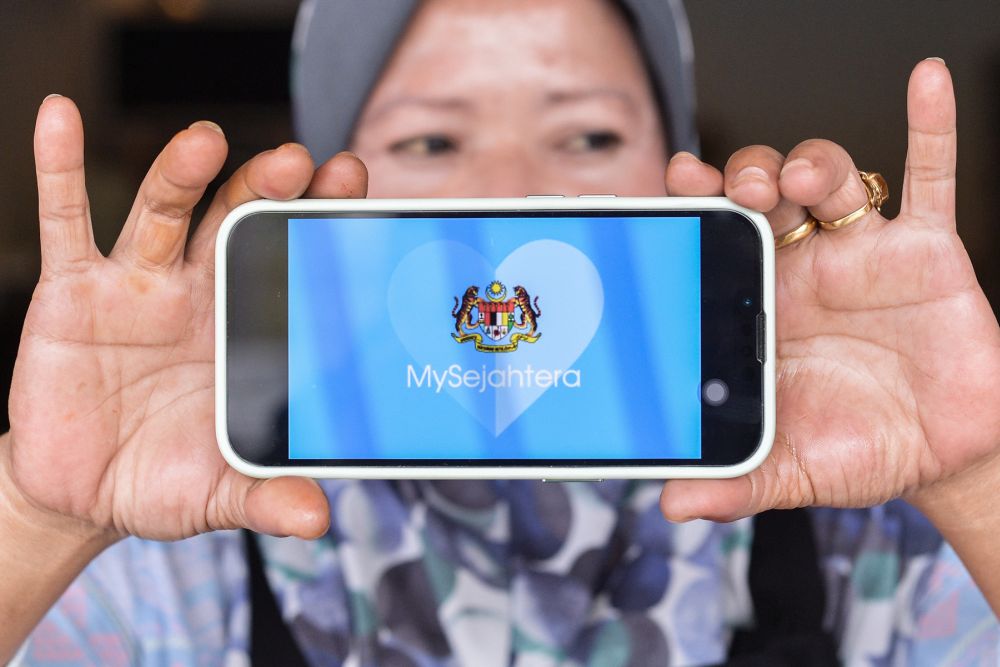 A woman holds up a phone displaying the MySejahtera app in Shah Alam March 31, 2022. u00e2u20acu201d Picture by Miera Zulyana