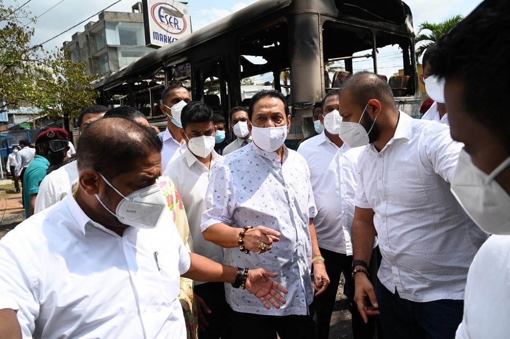 Sri Lankau00e2u20acu2122s Prime Minister Mahinda Rajapaksa (centre) is escorted past a burnt bus at the site of last night protest outside Sri Lankan presidentu00e2u20acu2122s home to call for his resignation, in Colombo April 1, 2022. u00e2u20acu201d AFP pic
