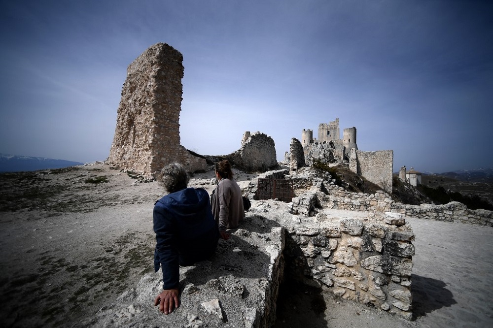 People sit by the castle of Rocca Calascio on March 29, 2022. — AFP pic