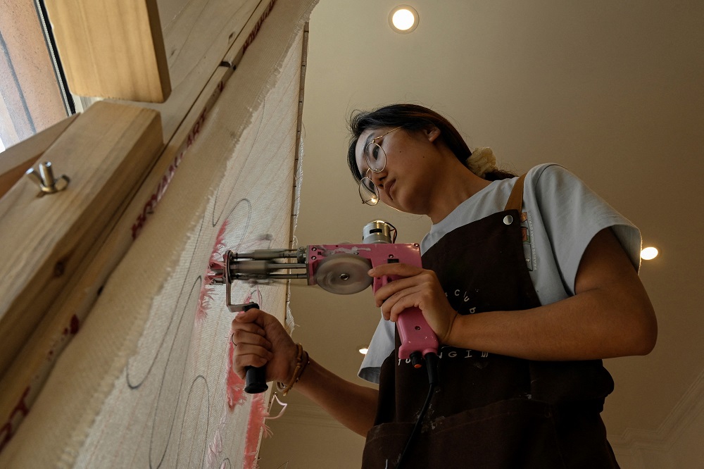A staff member using a craft gun to create patterns on stretched fabric at a tufting workshop in Beijing. u00e2u20acu201d AFP pic
