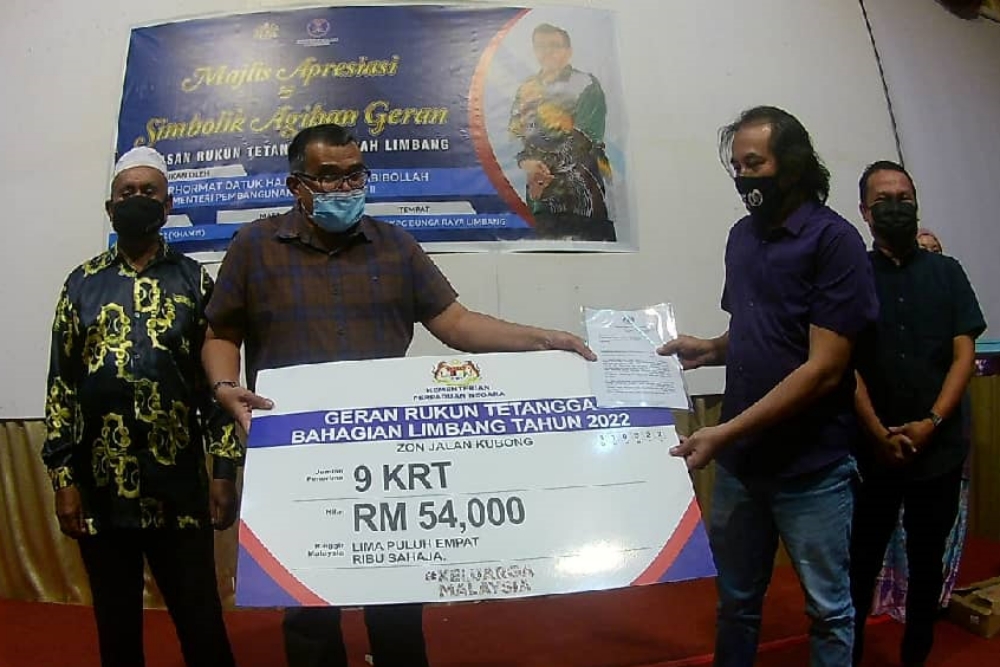 Hasbi (second left) presents a mock cheque to Roslan Ismail the chairman of KRT Kuala Berawan Limbang while Fakri (right) looks on. u00e2u20acu2022 Borneo Post pic