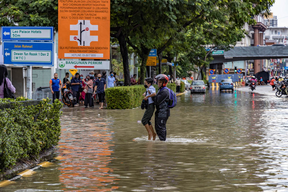A man carries a child to safety after the evening downpour in Kuala Lumpur, April 25, 2022. — Picture by Firdaus Latif