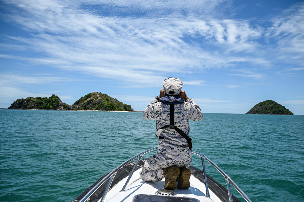 A member of the Malaysian Maritime Enforcement Agency uses binoculars during the search to locate three divers at sea April 8, 2022 in Johor. u00e2u20acu201d AFP pic 
