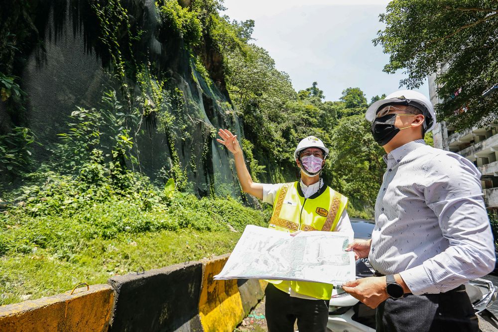Penang exco Zairil Khir Johari (right) looks at the rockfall netting covering hilly terrain along Lorong Bukit Kukus in Paya Terubong April 25, 2022. u00e2u20acu201d Picture by Sayuti Zainudinnn