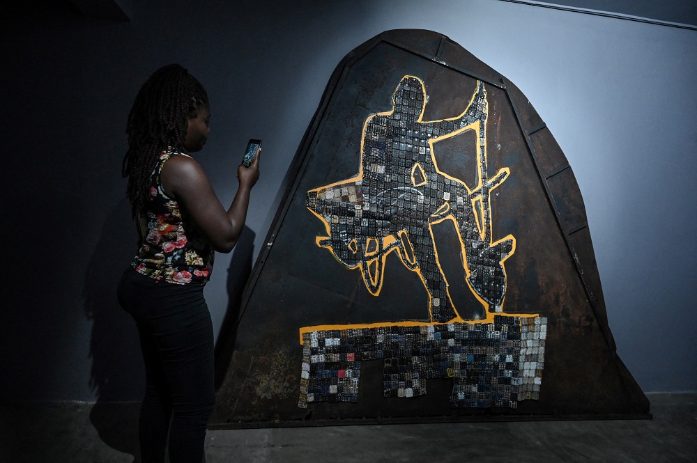 A woman films an artwork by Ivorian artist Mounou Du00c3u00a9siru00c3u00a9 Koffi during his exhibition opening at the Donwahi foundation in Abidjan April 29, 2022. u00e2u20acu201d AFP pic