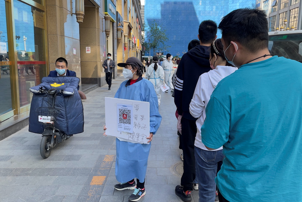 A worker in a protective suit holds a health QR code next to a line of people waiting for a nucleic acid test at a mass testing site for the coronavirus disease amid the outbreak, during the Labour Day holiday in Beijing, China May 1, 2022. u00e2u20acu201d AFP pic