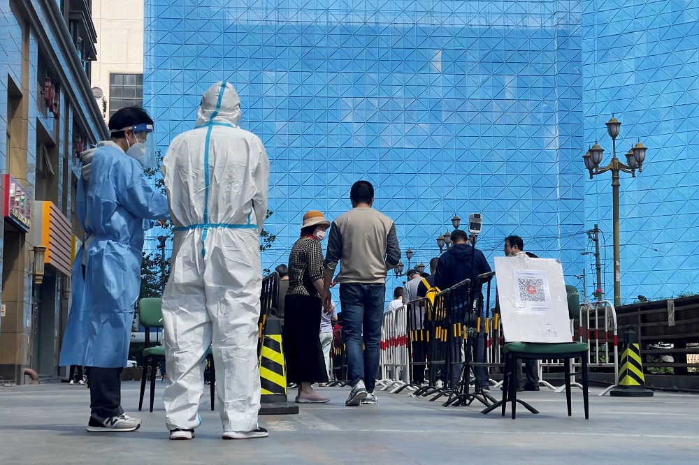 Workers in protective suits stand next to people lining up a makeshift nucleic acid testing site during a mass testing for Covid-19 in Chaoyang district of Beijing, China May 4, 2022. u00e2u20acu2022 Reuters pic