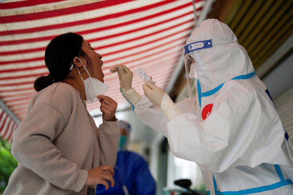 A medical worker in a protective suit collects a swab sample from a resident for nucleic acid testing, outside a closed entrance of a building during lockdown, in Shanghai, China, May 12, 2022. u00e2u20acu2022 Reuters pic
