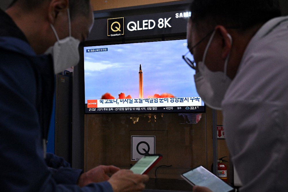 Two men check their phones as a television screen shows file footage of a North Korean missile test in Seoul on May 12, 2022, after Seoulu00e2u20acu2122s military said it had detected three short-range ballistic missiles fired from near Pyongyang. u00e2u20acu201d AFP pic