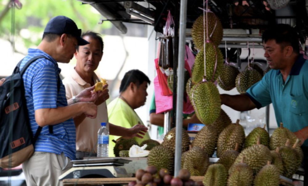Tourists enjoying durians sold at Anson Street, George Town, June 18, 2019. u00e2u20acu201d Bernama pic