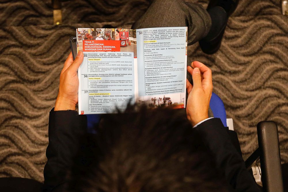 An attendee reads a copy of the Penang state governmentu00e2u20acu2122s 2018 general election manifesto report card at Komtar May 9, 2022. u00e2u20acu201d Picture by Sayuti Zainudin