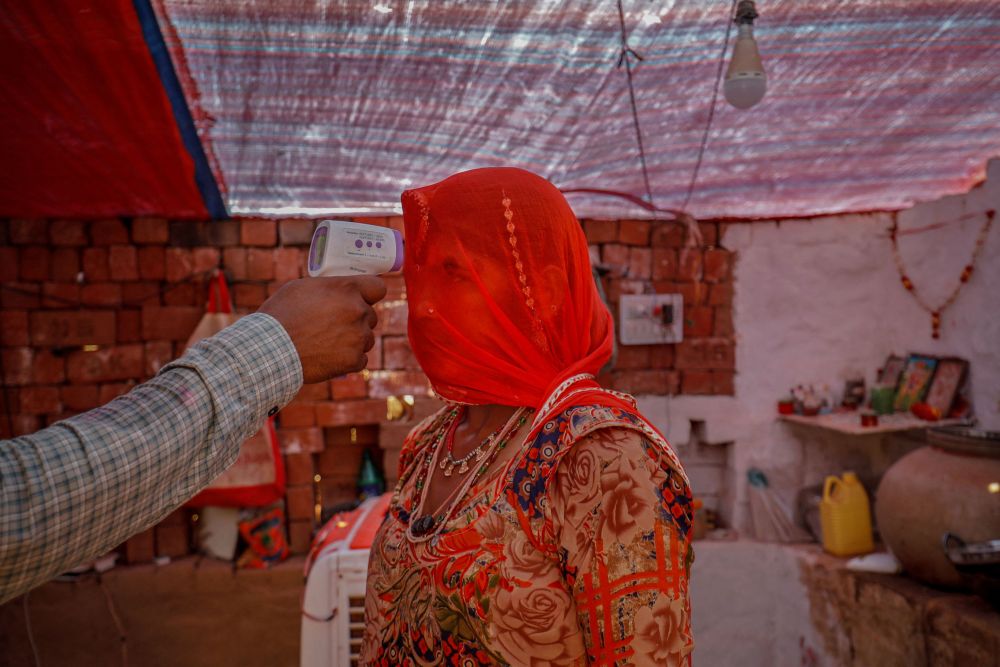 A healthcare worker checks the temperature of a woman inside her hut during a coronavirus disease vaccination drive for workers at a brick kiln in Kavitha village on the outskirts of Ahmedabad, Indi, April 8, 2021. u00e2u20acu201d Reuters pic