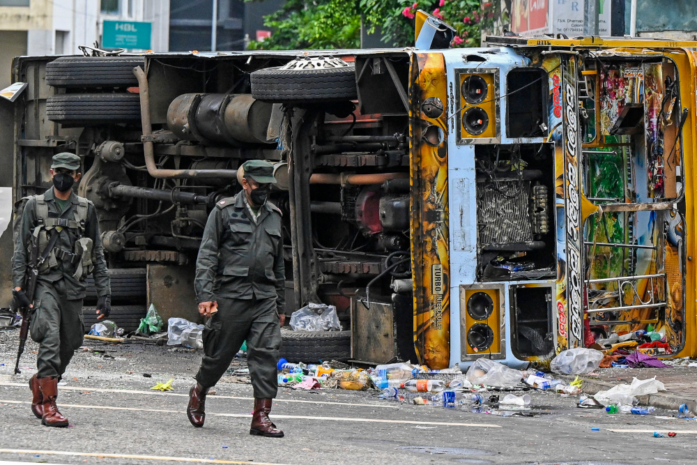 Security personnel walk past a burned vehicle along a road, a day after they were torched by protesters in Colombo, May 10, 2022. u00e2u20acu201d AFP pic 