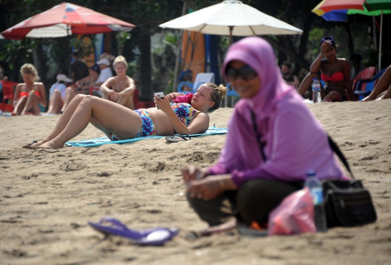 A Muslim woman wearing a veil sits in front of foreign tourists wearing bikinis on Kuta beach in Bali on June 6, 2013. u00e2u20acu201d AFP pic
