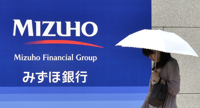 A woman walks in front of a signboard of Japan's Mizuho Financial Group in Tokyo on May 15, 2013.u00e2u20acu201d AFP pic