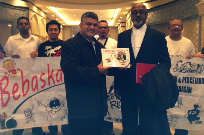 Cartoonist Zunar (front left) poses with his lawyer Sivarasa Rasiah (right) and a copy of the comic book for which he was arrested in 2010. u00e2u20acu201d Picture by Melissa Chi